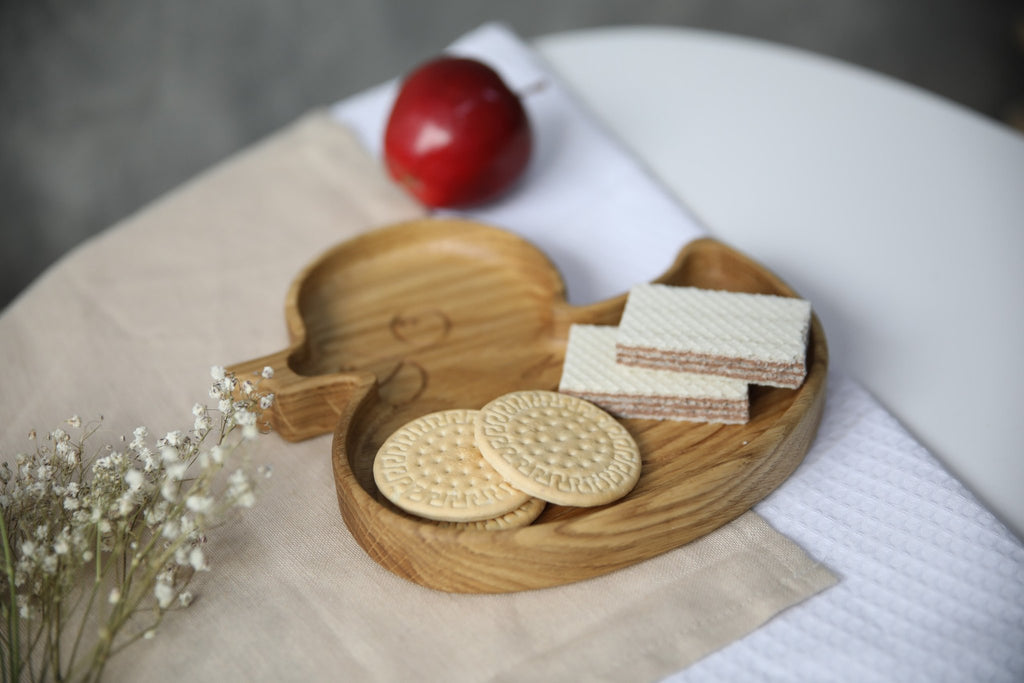 3. Side view of wooden duckling plate with cookies and wafers, placed on a beige cloth with a red apple and white flowers