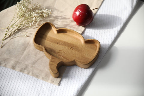 4. Wooden elephant-shaped plate on a textured fabric with a red apple and dried flowers