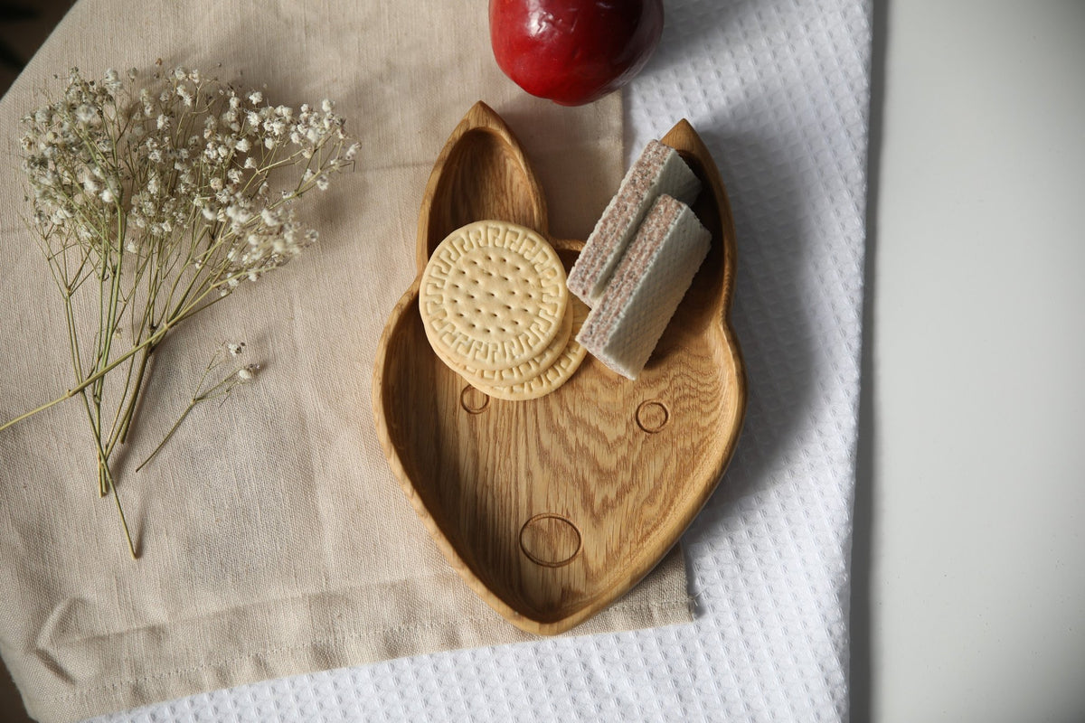 1. Handmade wooden fox-shaped plate with cookies and wafers on a beige cloth, next to a red apple and white flowers