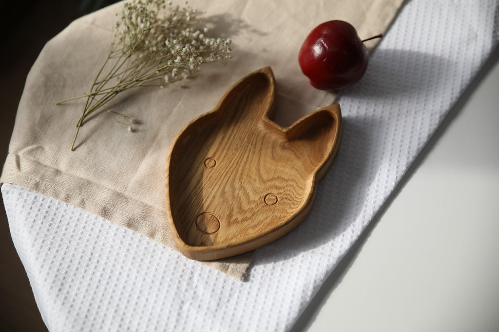 3. Wooden fox-shaped plate on beige cloth with red apple and white flowers, showing smooth surface and engraved details