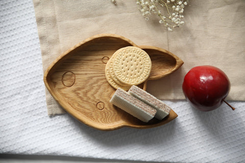 5. Wooden fox-shaped plate with cookies and wafers on beige cloth, next to a red apple and white flowers