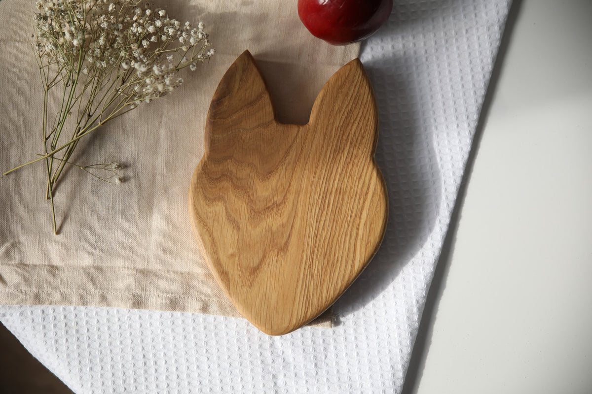2. Back view of wooden fox-shaped plate on beige cloth with red apple and white flowers