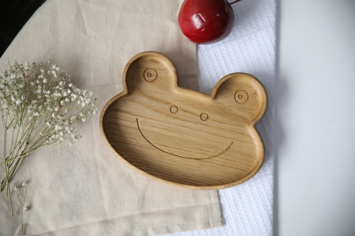 1. Handmade wooden frog-shaped plate on beige fabric with red apple and white flowers, showcasing smooth finish