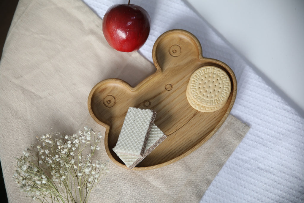 8. Wooden frog plate with cookies and wafers, red apple, and white flowers on beige fabric, showcasing functionality