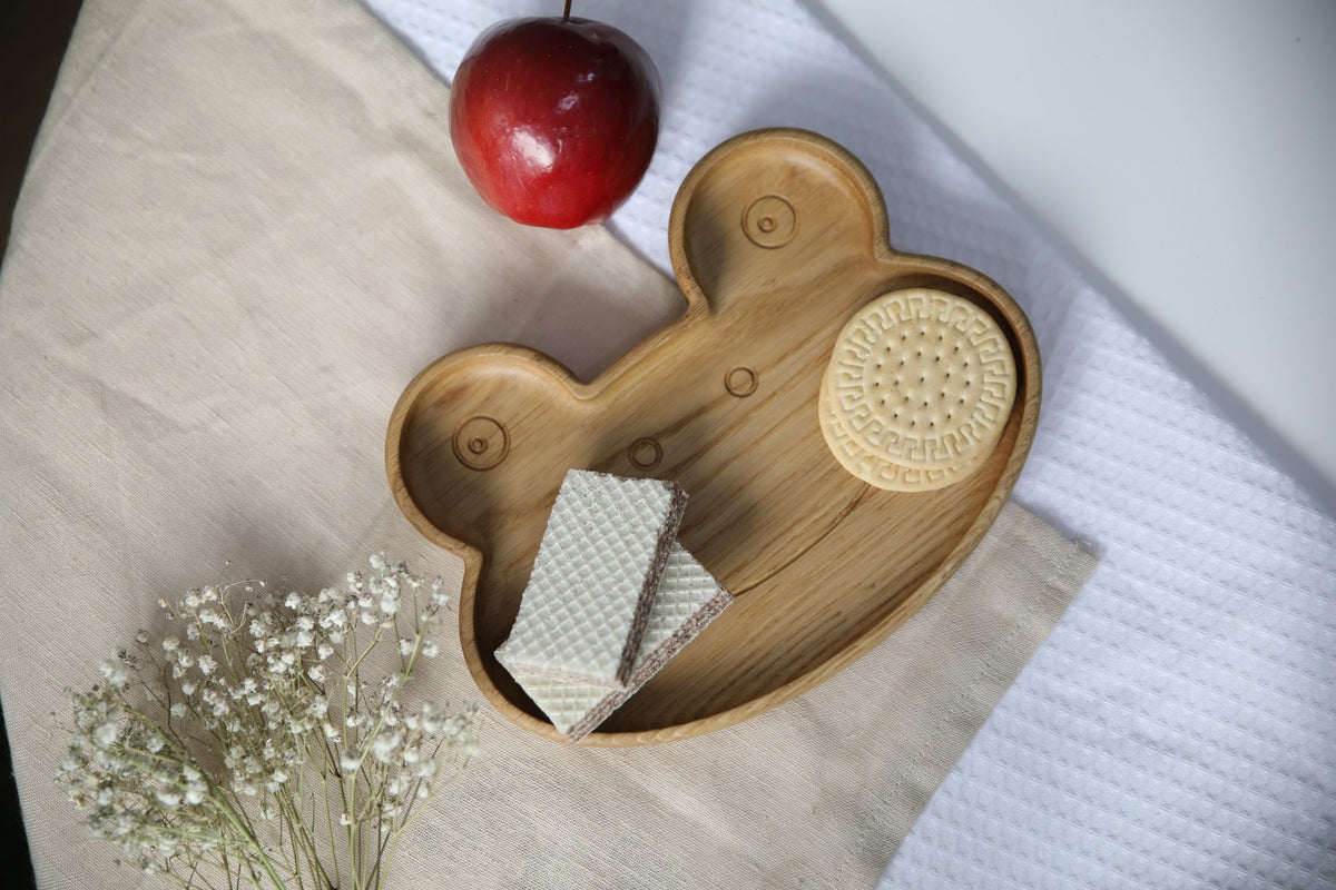 8. Wooden frog plate with cookies and wafers, red apple, and white flowers on beige fabric, showcasing functionality