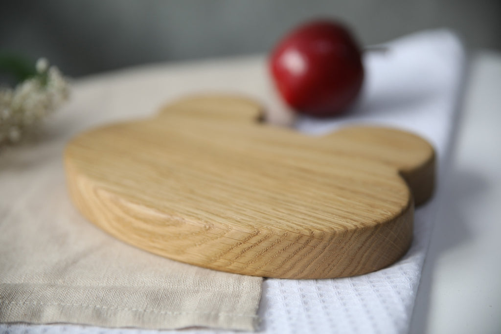 7. Side angle of wooden frog plate on beige fabric with red apple, highlighting thickness and craftsmanship