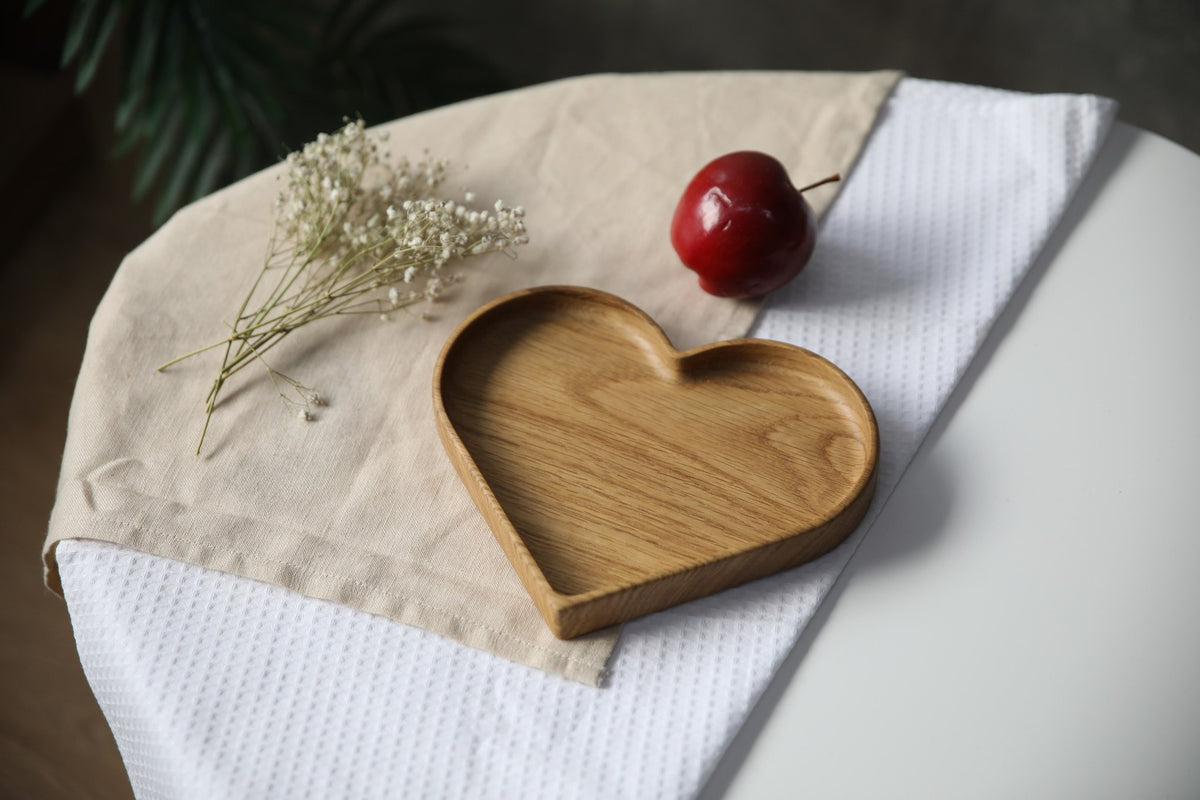 3. Heart-shaped wooden plate on white and beige cloth with red apple and dried flowers, highlighting natural wood grain