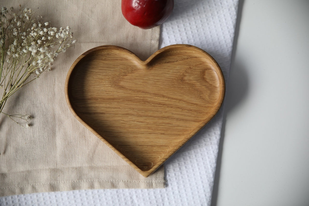 2. Heart-shaped wooden plate on beige cloth with red apple and white flowers, showcasing smooth oak finish