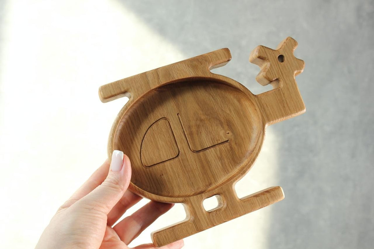 7. Hand holding a wooden helicopter-shaped plate for kids, made of oak or ash, with a smooth finish, against a light background