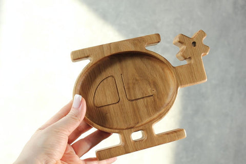 1. Hand holding a handmade wooden helicopter-shaped plate for kids, made of oak or ash, with a smooth finish, shown against a light background
