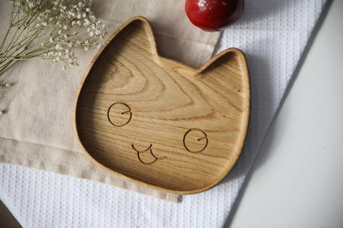 1. Handmade wooden plate for kids in cat shape on a textured cloth with flowers and an apple, showcasing smooth oak finish