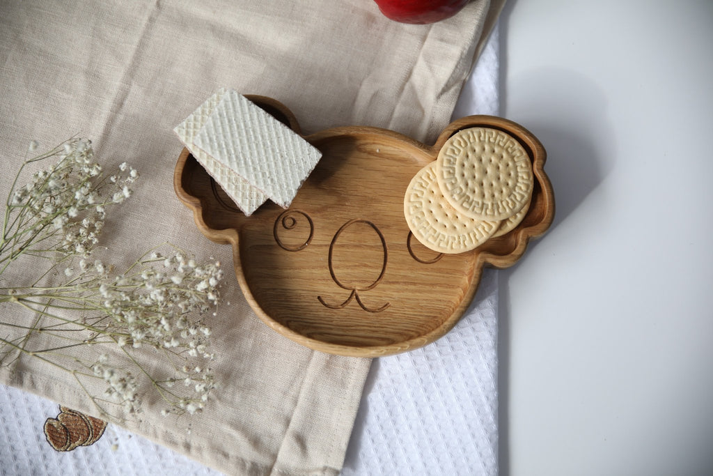 7. Wooden koala-shaped plate on beige cloth with wafers and cookies, highlighting engraved face and smooth oak finish