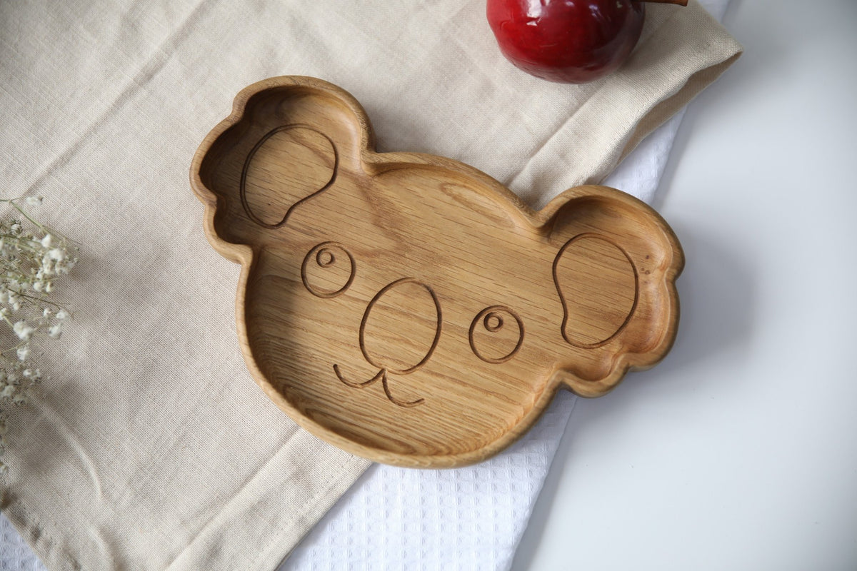 1. Handmade wooden koala-shaped plate on a beige cloth with a red apple, showcasing smooth oak finish and engraved face design