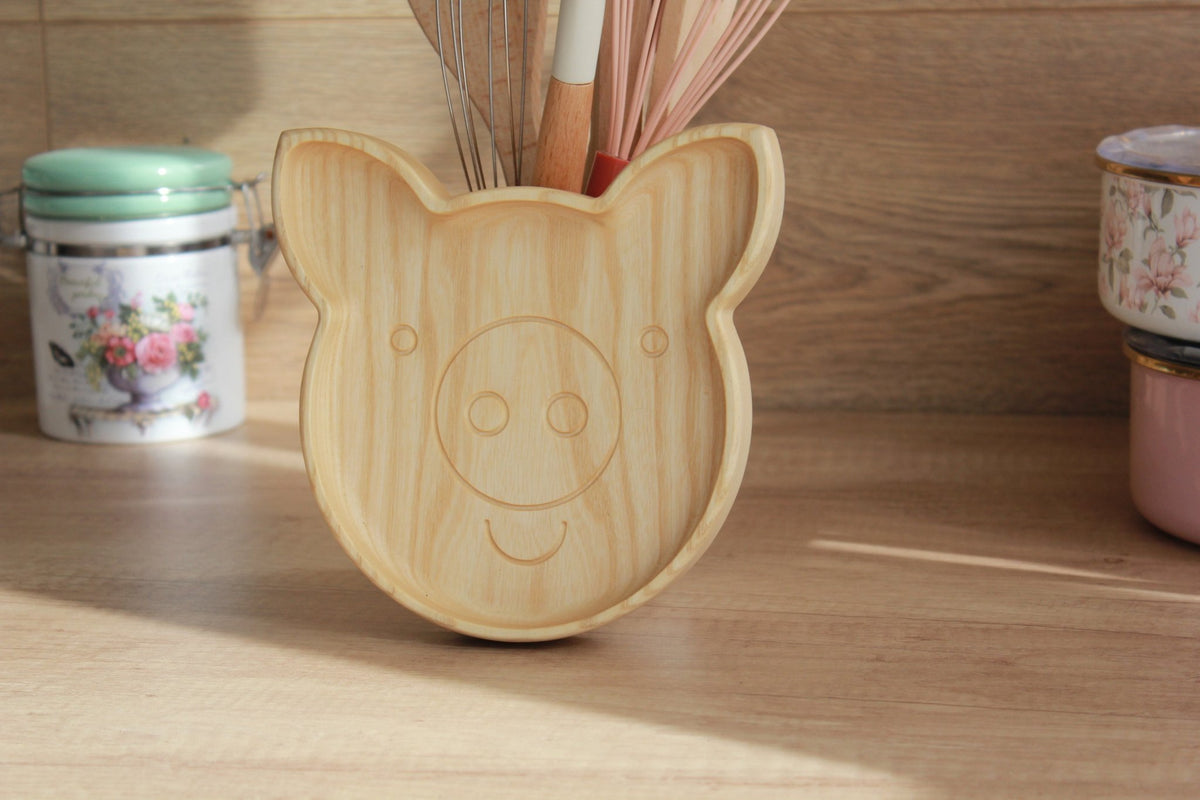 2. Wooden pig-shaped plate standing on a kitchen counter with floral tins in the background