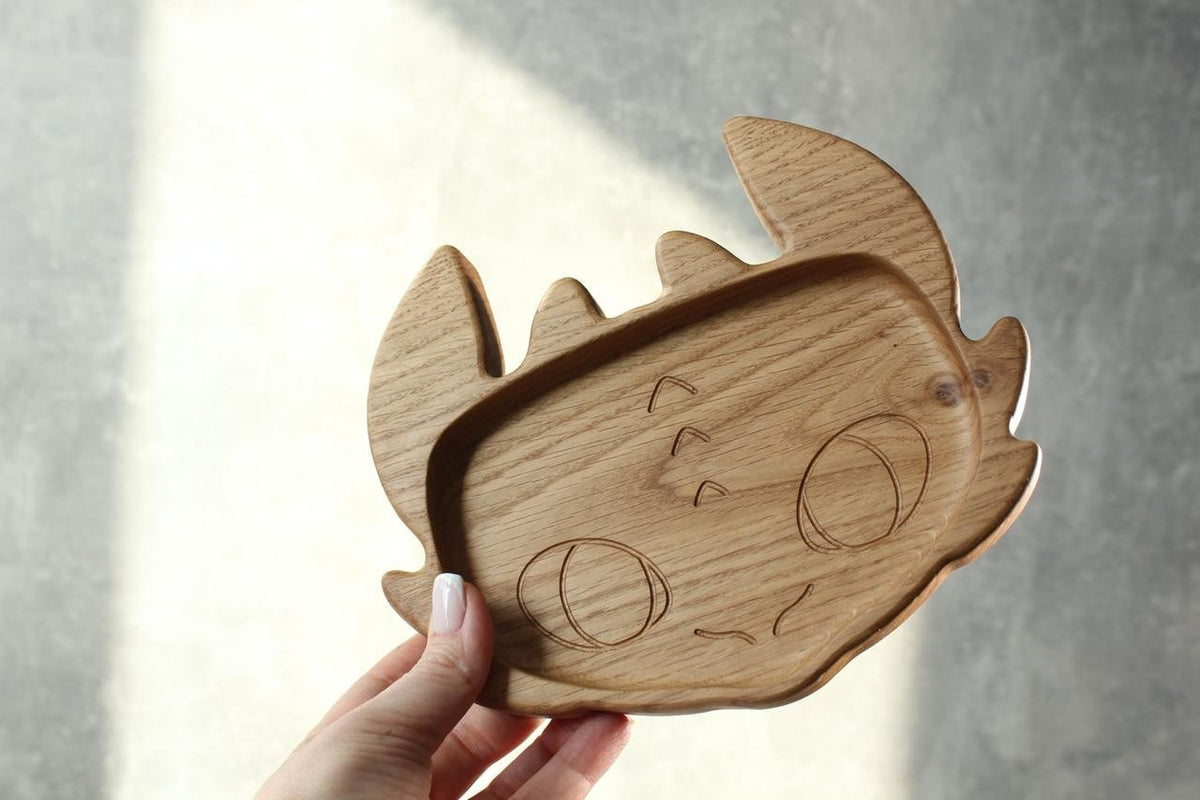 4. Person holding a handmade wooden kids plate shaped like a character face, crafted from oak wood, against a grey background