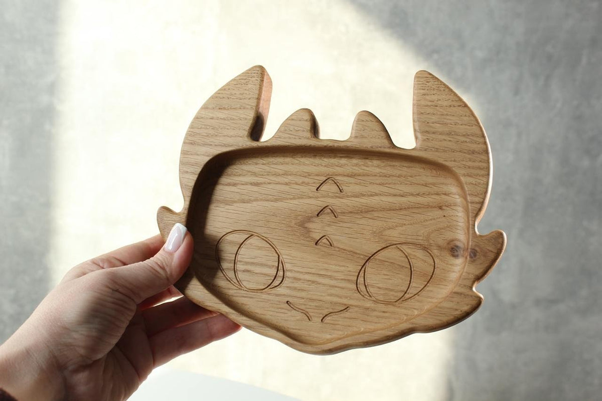 2. Person holding a handmade wooden kids plate shaped like a character face, crafted from oak wood, in natural lighting