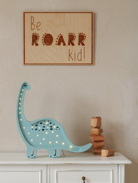 2. Engraved 'Be Roarr Kid' wooden poster on wall above white cabinet with blue dinosaur lamp and wooden blocks
