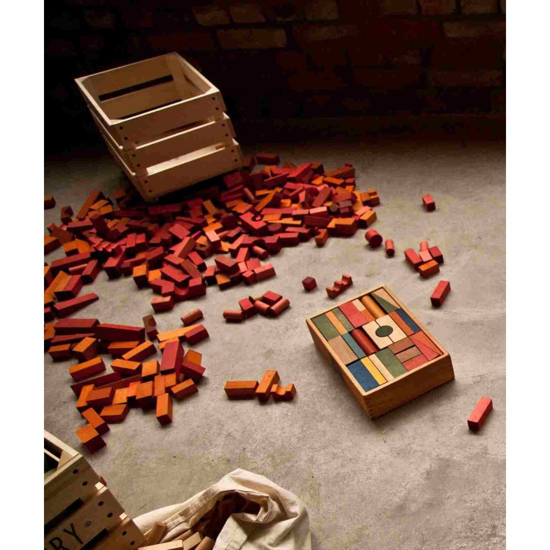 3. Scattered Wooden Story warm-colored wooden blocks on a concrete floor with a wooden box and bag nearby