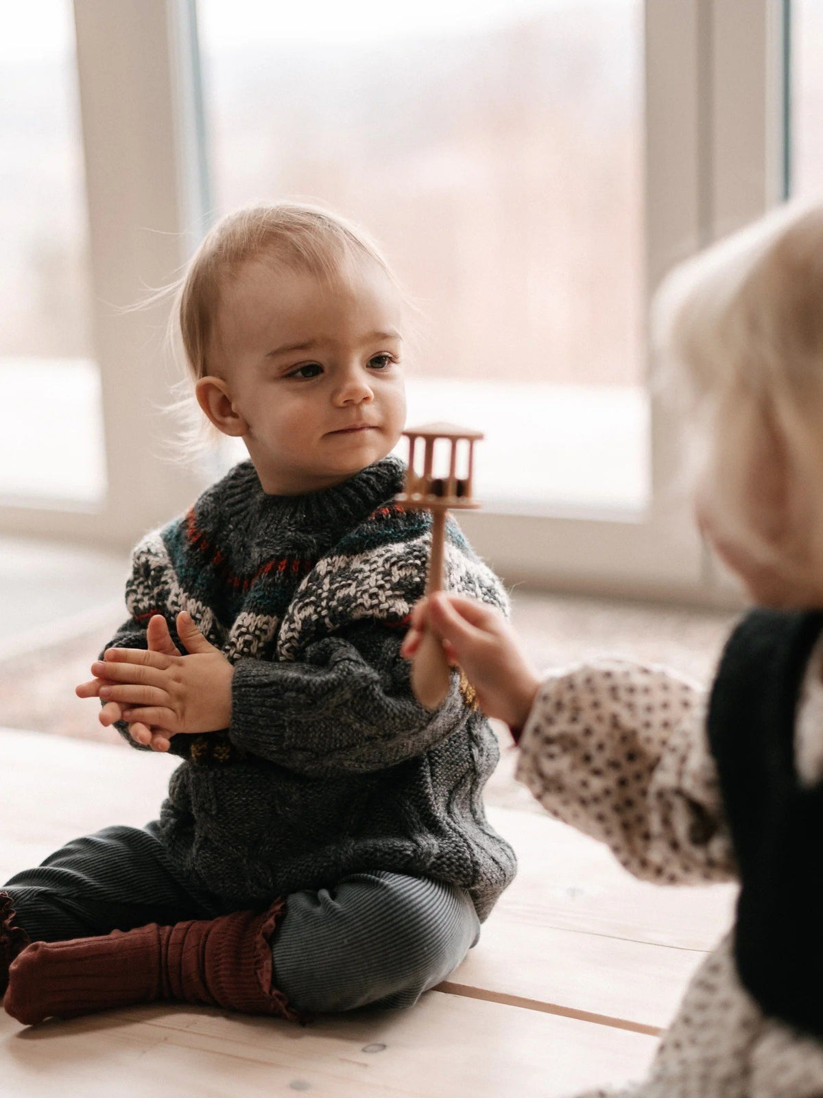 5. Two children sitting on the floor, one offering a Wooden Story rattle to the other