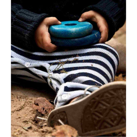 4. Close-up of child's hands holding blue wooden disks from the round pyramid toy, wearing striped pants and black sweater, sitting on the ground