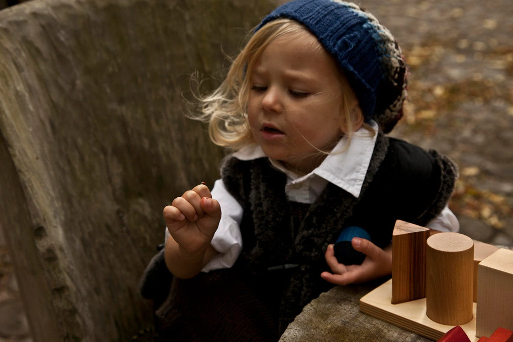 1. Child playing with wooden shape sorting blocks outdoors, wearing a blue knit hat and dark vest