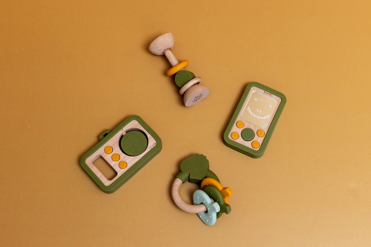 4. Flat lay of Trixie Baby's wooden silicone camera, rattle, and toy phone on mustard background, highlighting playful design and color scheme
