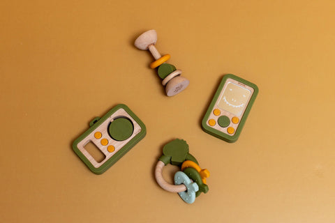 4. Flat lay of Trixie Baby's wooden silicone camera, rattle, and toy phone on mustard background, highlighting playful design and color scheme
