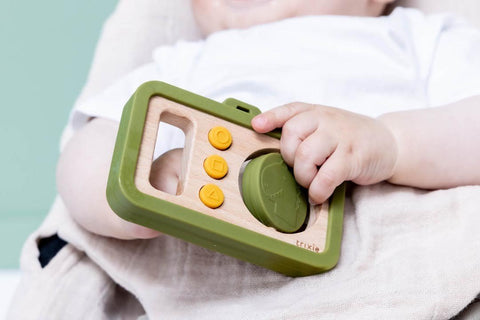1. Baby holding Trixie Baby's wooden silicone camera with green frame and yellow buttons, showcasing easy grip and playful design
