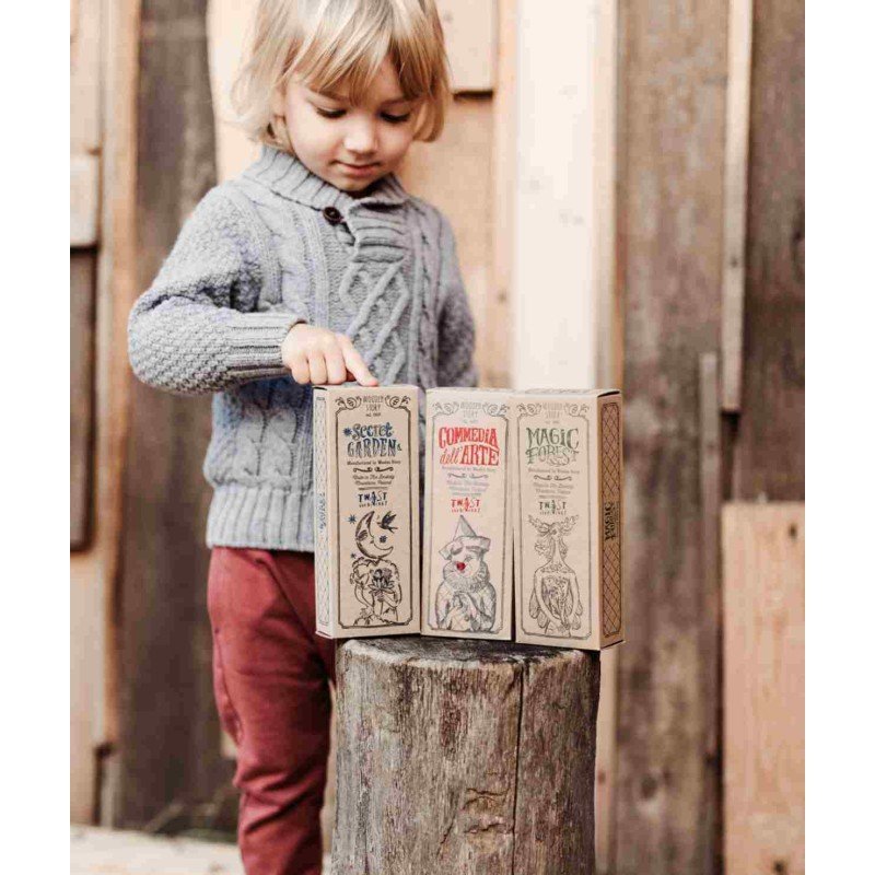 6. Child in grey sweater pointing at three boxed wooden puzzles on tree stump
