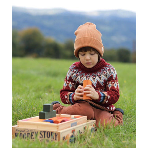1. Child in knit sweater and beanie playing with Wooden Story wooden wagon and blocks on grass