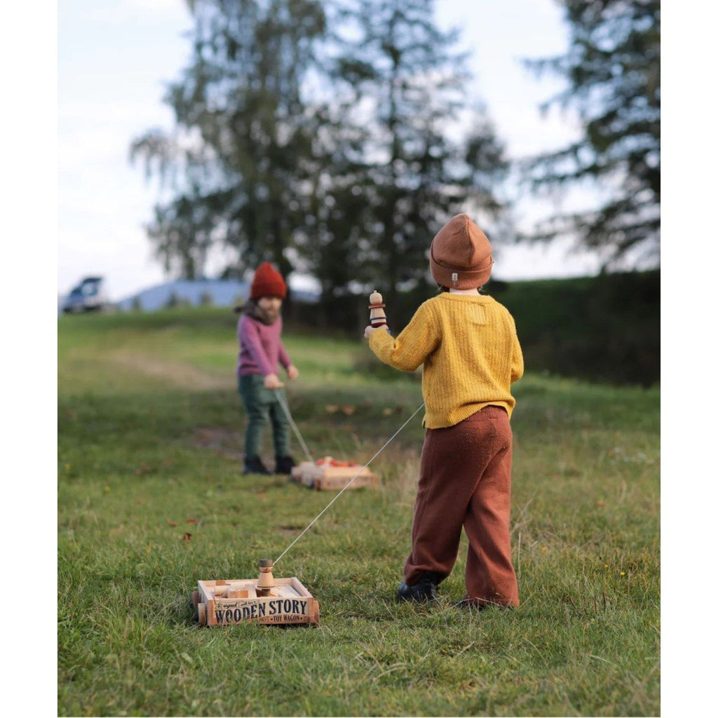 1. Two children playing with Wooden Story wooden wagons in a grassy outdoor setting