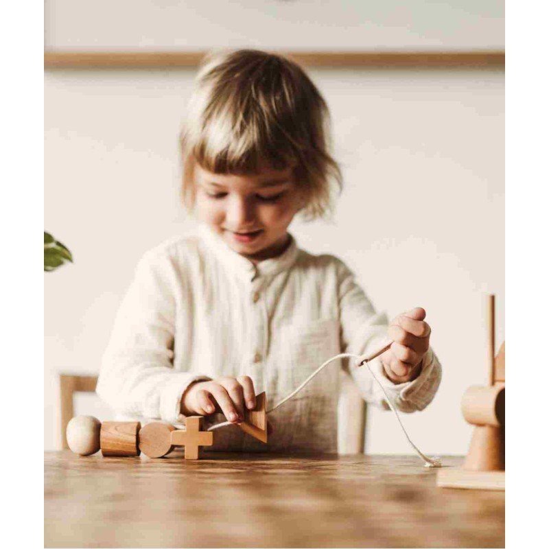 1. Child threading wooden blocks with Wooden Story needle on a table