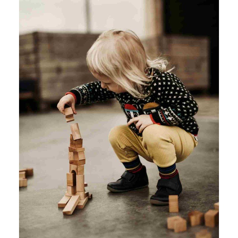 1. Child crouching and stacking wooden blocks on the floor, wearing patterned sweater and yellow pants