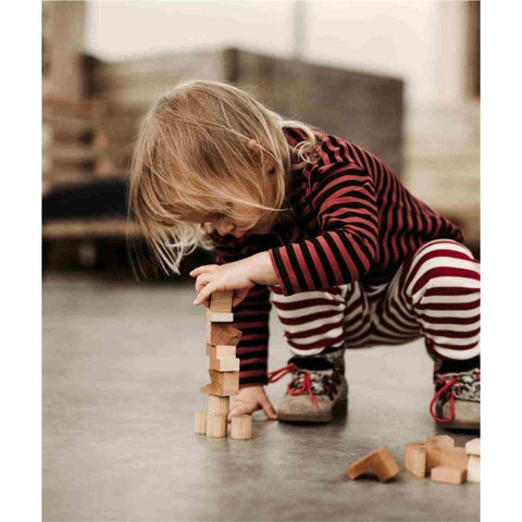 1. Child in striped outfit building with Wooden Story natural wooden tower puzzle blocks on the floor