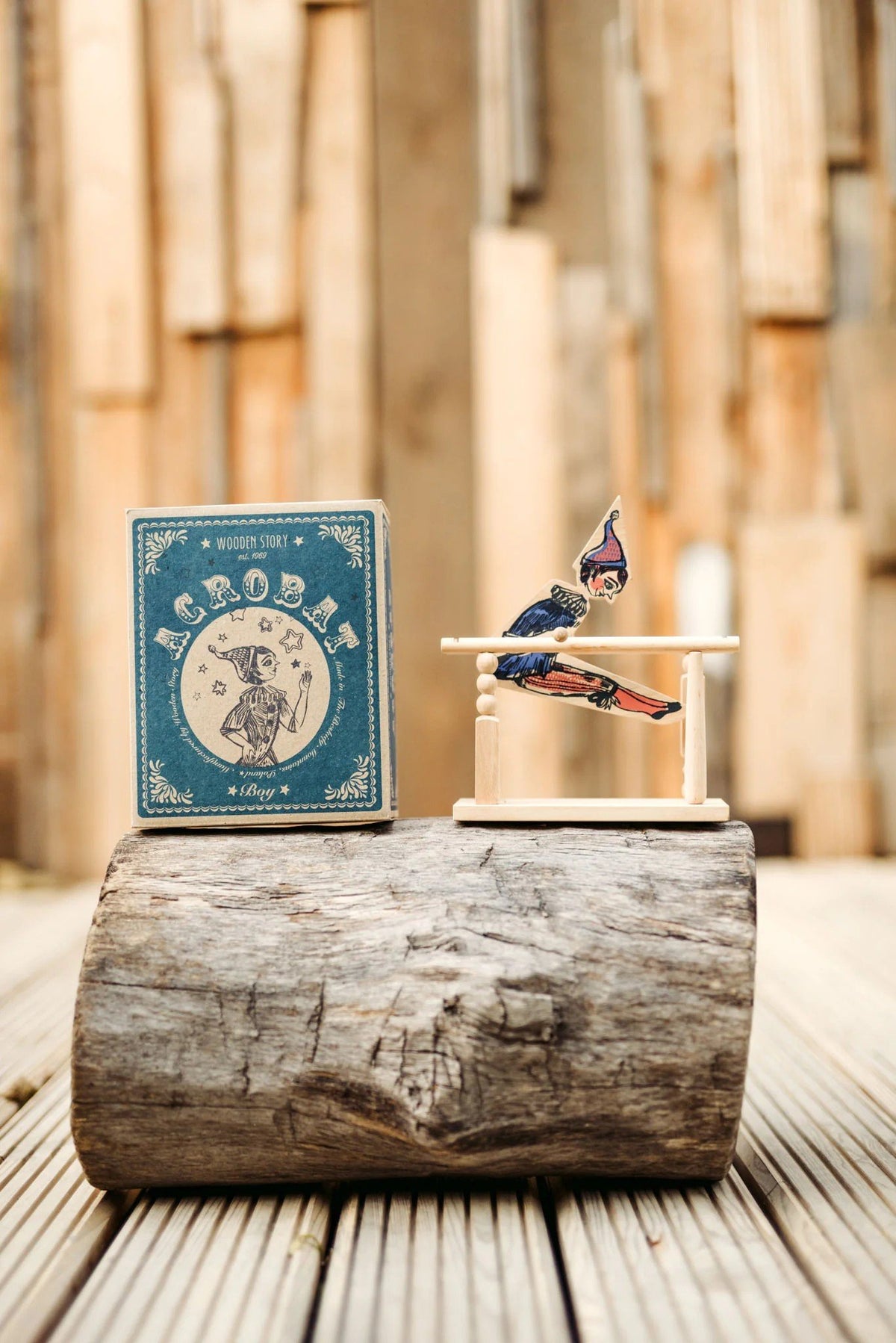 1. Wooden Story acrobat toy and box displayed on a wooden log with a rustic background