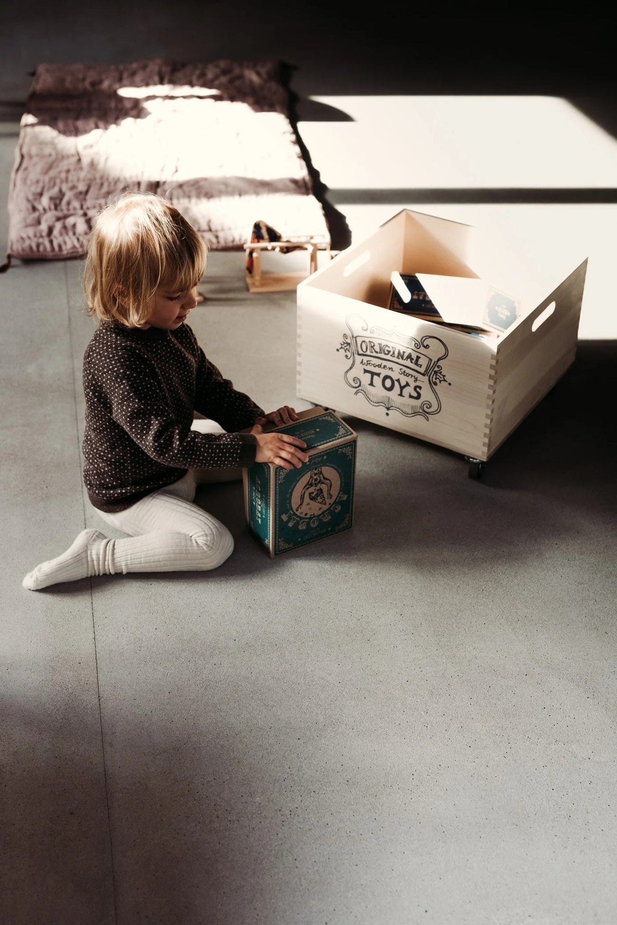 1. Child sitting on the floor with Wooden Story acrobat toy box, next to a wooden toy crate in a bright room