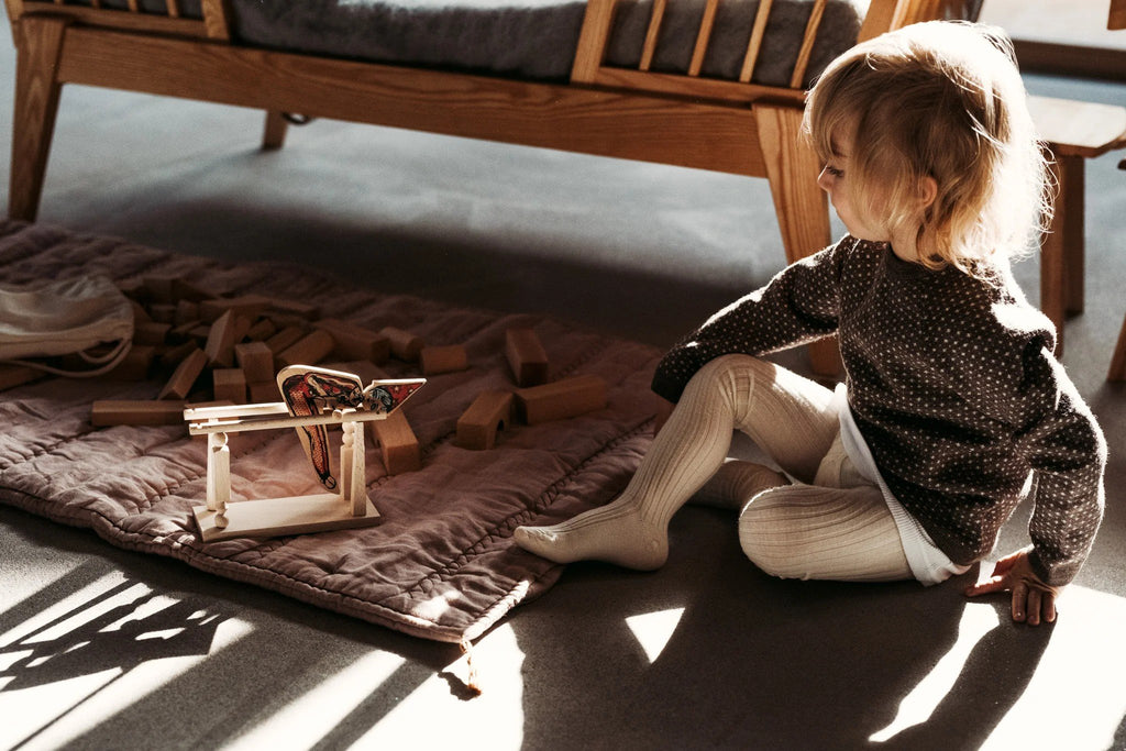 1. Child sitting on the floor, playing with Wooden Story acrobat toy in a sunlit room