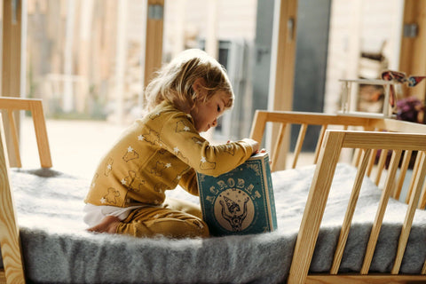 1. Child in yellow pajamas sitting on a bed, engaging with the Wooden Story acrobat toy box in a cozy room
