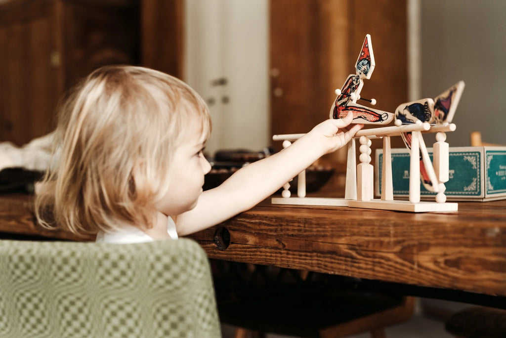 1. Child playing with Wooden Story acrobat toy on a wooden table, focusing on the toy's movement