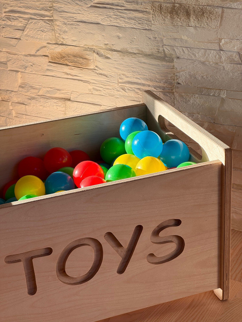 3. Close-up of wooden toy box filled with colorful balls showing 'TOYS' cutout and smooth handle