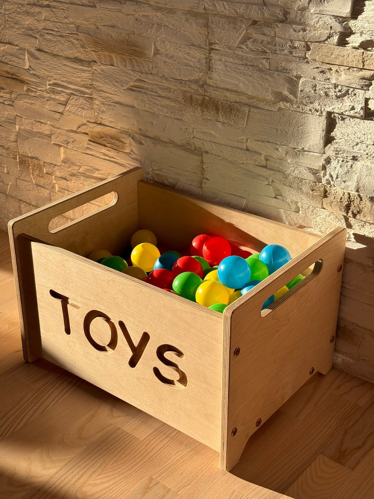 1. Wooden toy box with 'TOYS' cutout filled with colorful balls against a stone wall in a sunlit room