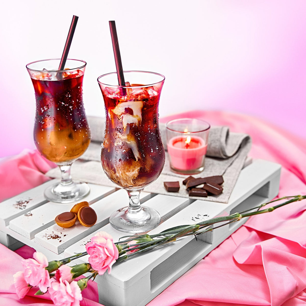 1. Two glasses of iced coffee on a white wooden tray with pink flowers and a candle