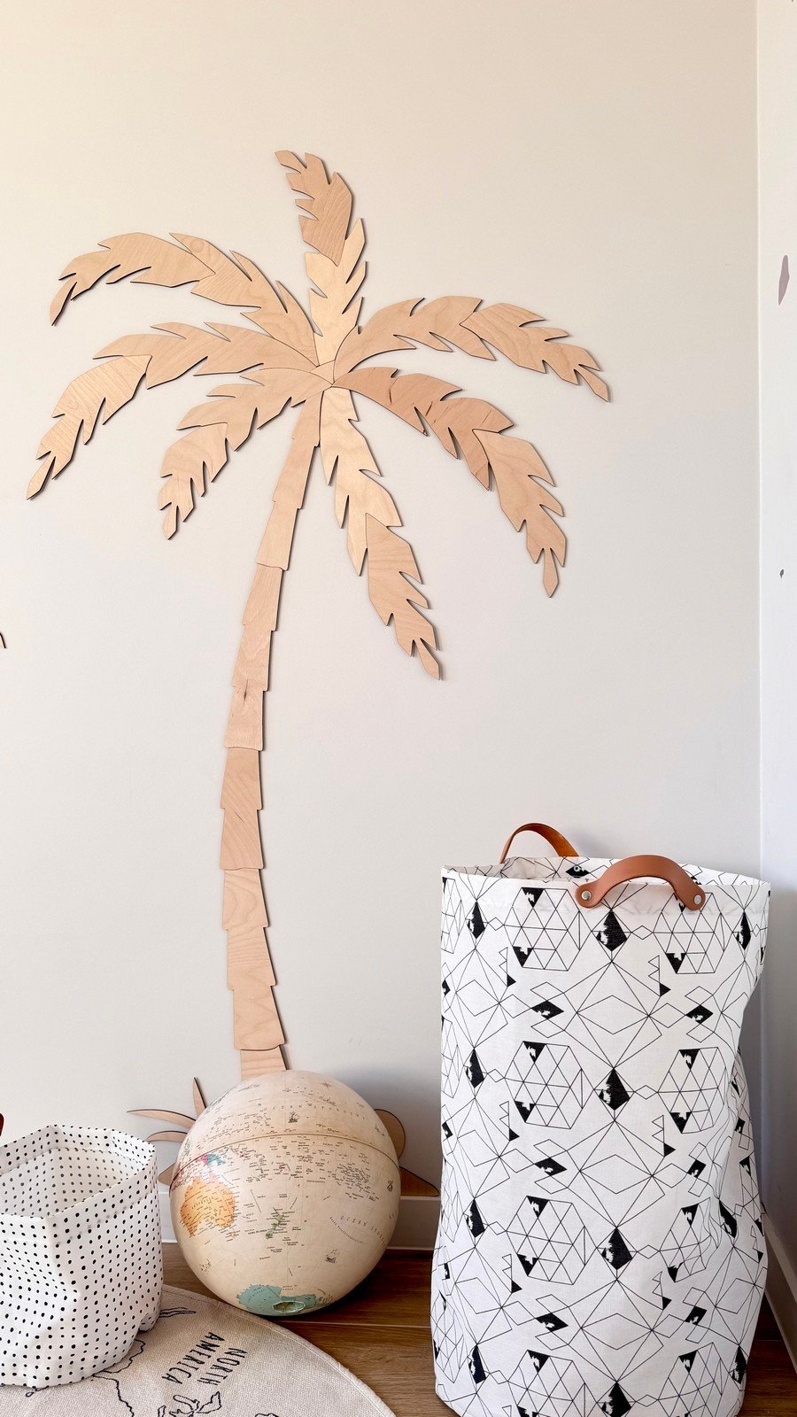 4. Single wooden palm tree wall decor in children's room, natural plywood, with a patterned storage basket and globe nearby