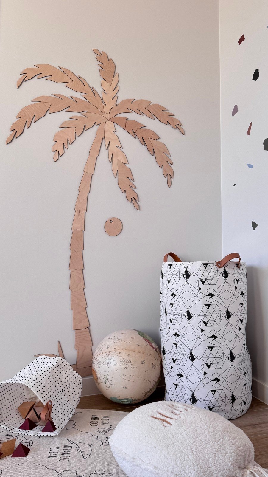 3. Close-up of large wooden palm tree wall decor in children's room, natural plywood, next to a patterned storage basket and globe