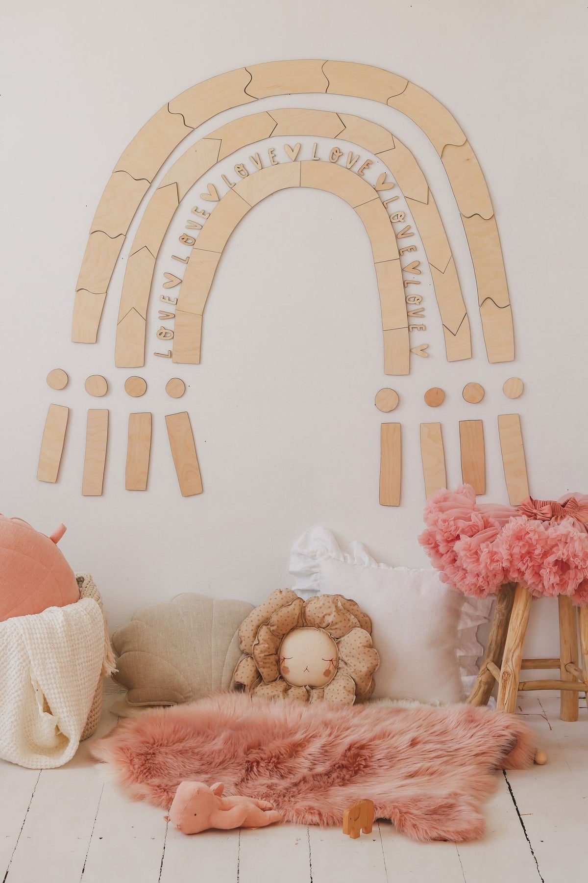 7. Wooden rainbow puzzle wall decoration in a child's room with pink and beige cushions, enhancing a whimsical atmosphere