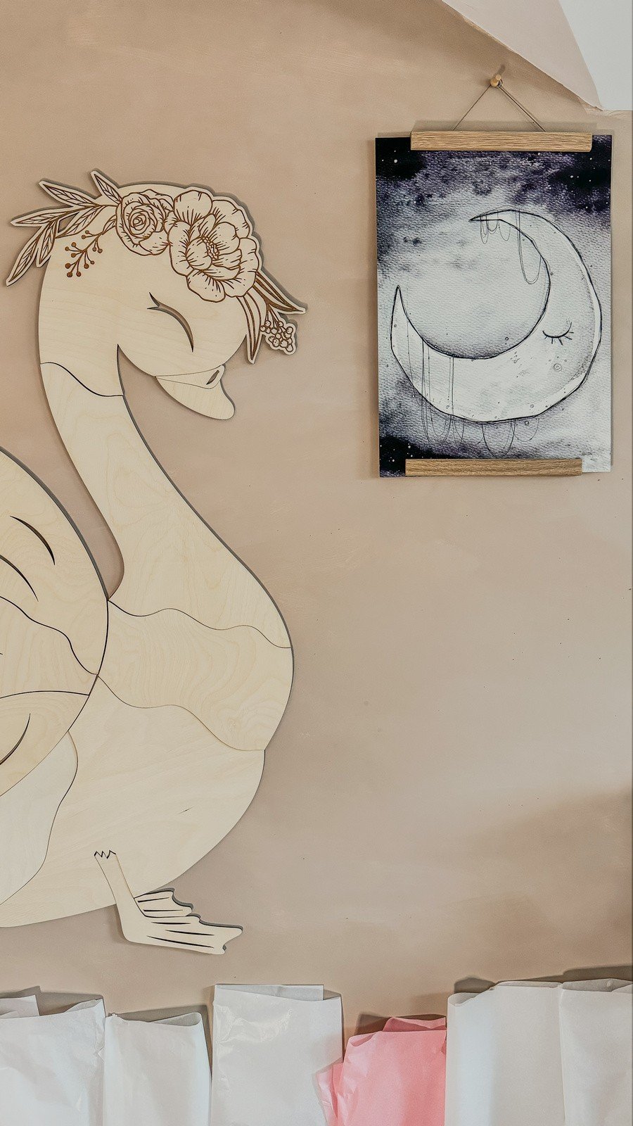2. Wooden swan wall decoration next to a moon-themed artwork on a beige wall