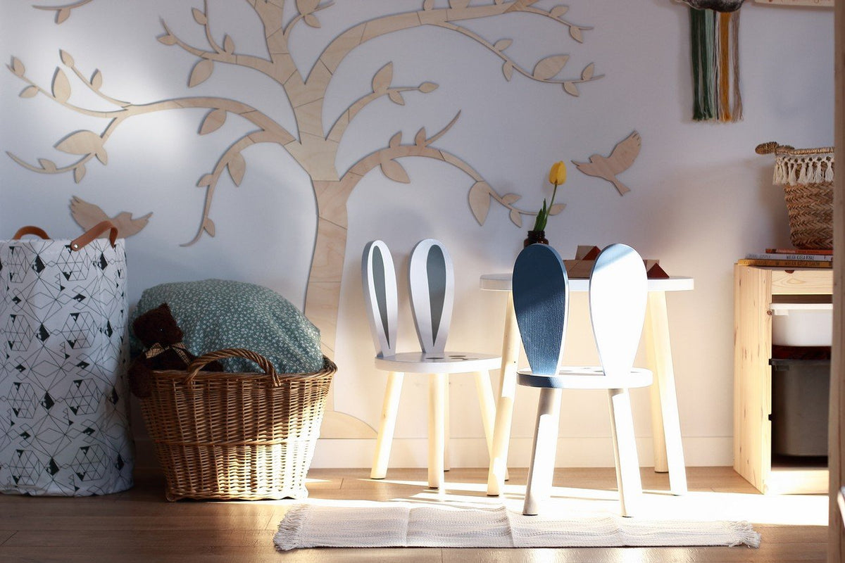 7. Wooden tree wall art with birds in a room with a basket and children's table, enhancing a warm and creative atmosphere.
