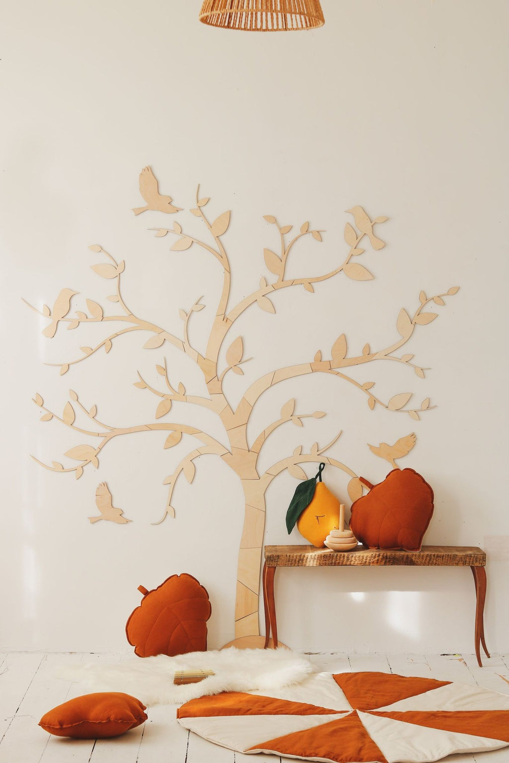 1. Wooden wall decoration of a tree with birds in a cozy room with orange cushions and a bench, creating a warm and inviting atmosphere.