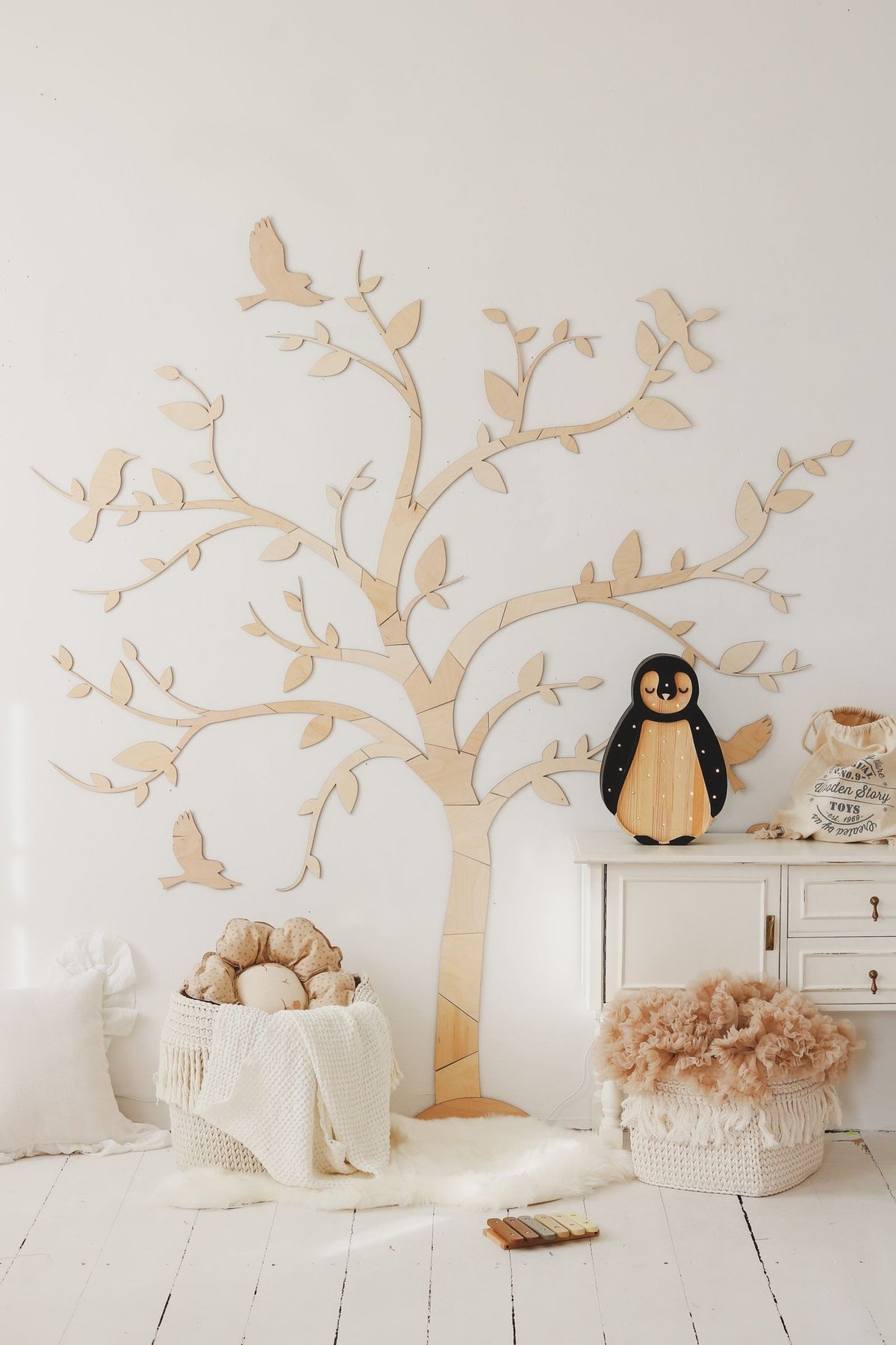 5. Wooden tree wall art with birds in a bright room with a penguin toy and soft furnishings, offering a cozy and charming look.