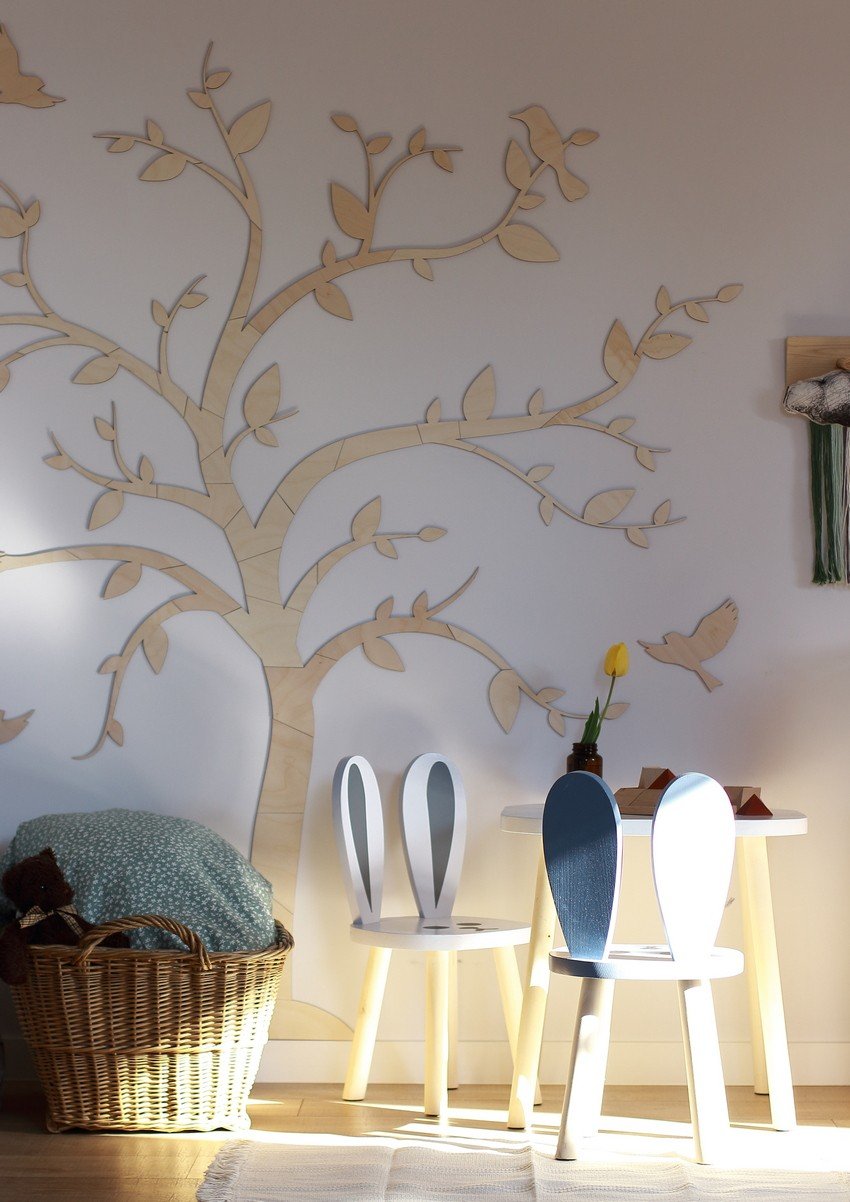 3. Wooden tree wall art with birds in a sunlit room with a basket and children's chairs, adding a natural touch to the decor.
